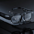 Black head-mounted smart Bluetooth glasses with a clear lens on a stand, showing the touch controls and recording camera.
