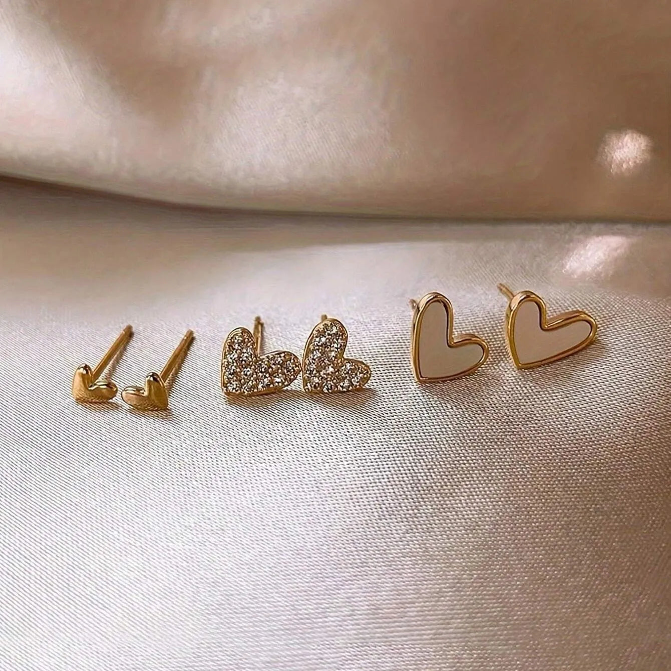 Three pairs of heart-shaped alloy earrings with electroplated finish in gold, black, pink or black and white