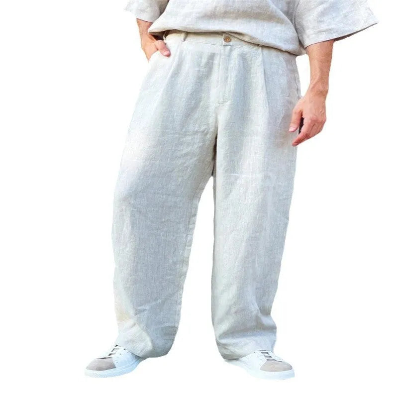 Men's loose linen high-waist jogger trousers in grey showing pleated detail and straight-leg fit