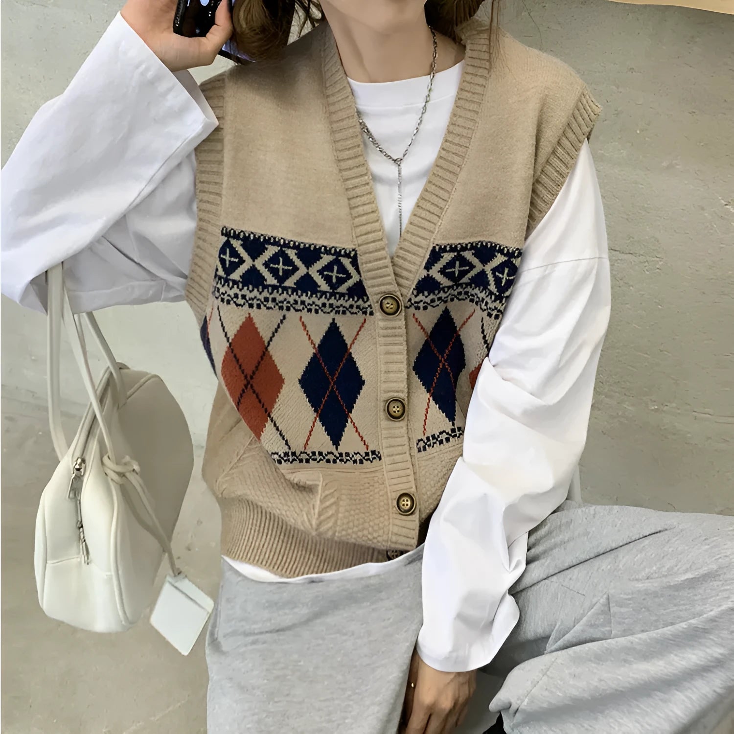Woman wearing a loose khaki diamond plaid sleeveless cardigan top over a white t-shirt.