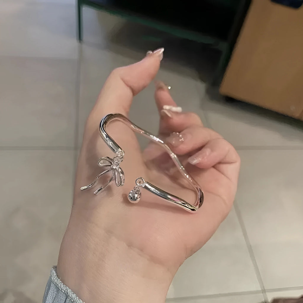 Close-up of a silver-toned adjustable bracelet with a bow bell charm on a model's wrist.