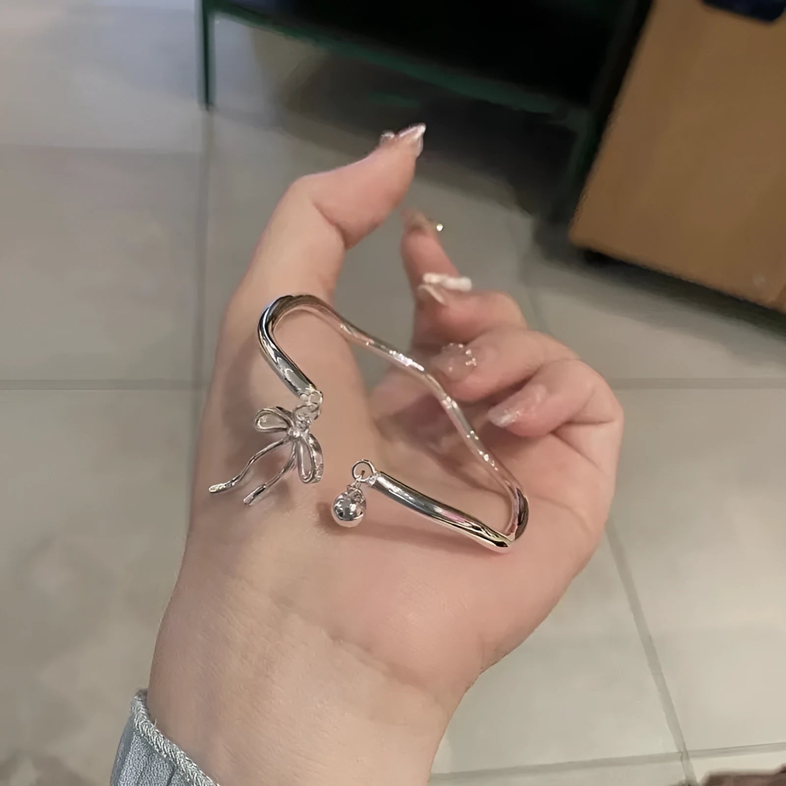 Close-up of a silver-toned adjustable bracelet with a bow bell charm on a model's wrist.
