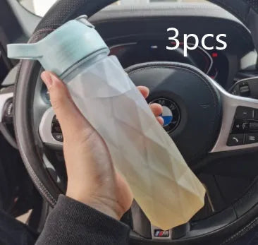 Large pink plastic spray water bottle with a handle strap and leakproof lid on a gym bag.