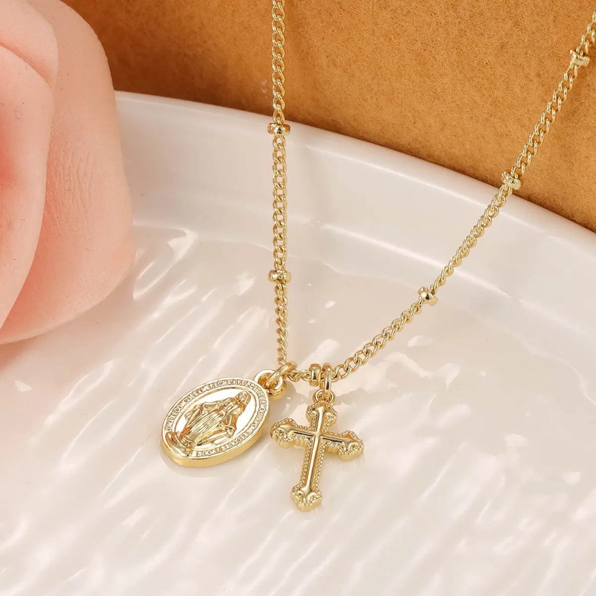 Geometric gold Virgin Mary cross pendant necklace on a chain.
