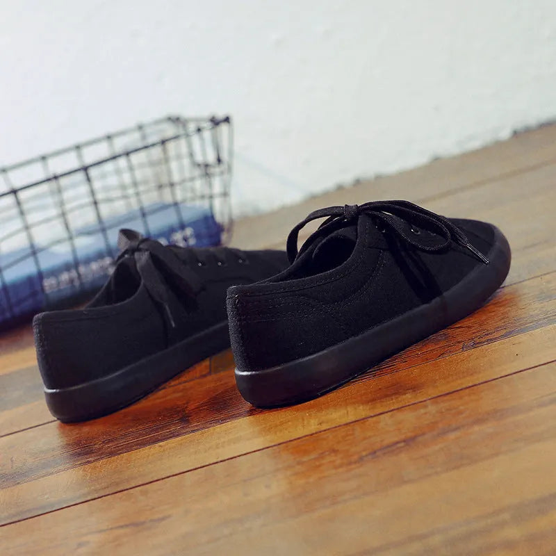 All-black women's low-top canvas shoes with lace-up front and flat rubber sole.