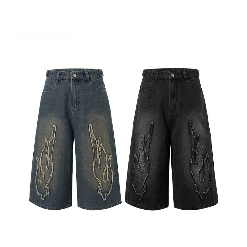 Man wearing black cropped denim shorts with a flame embroidery patch on the leg, street style.