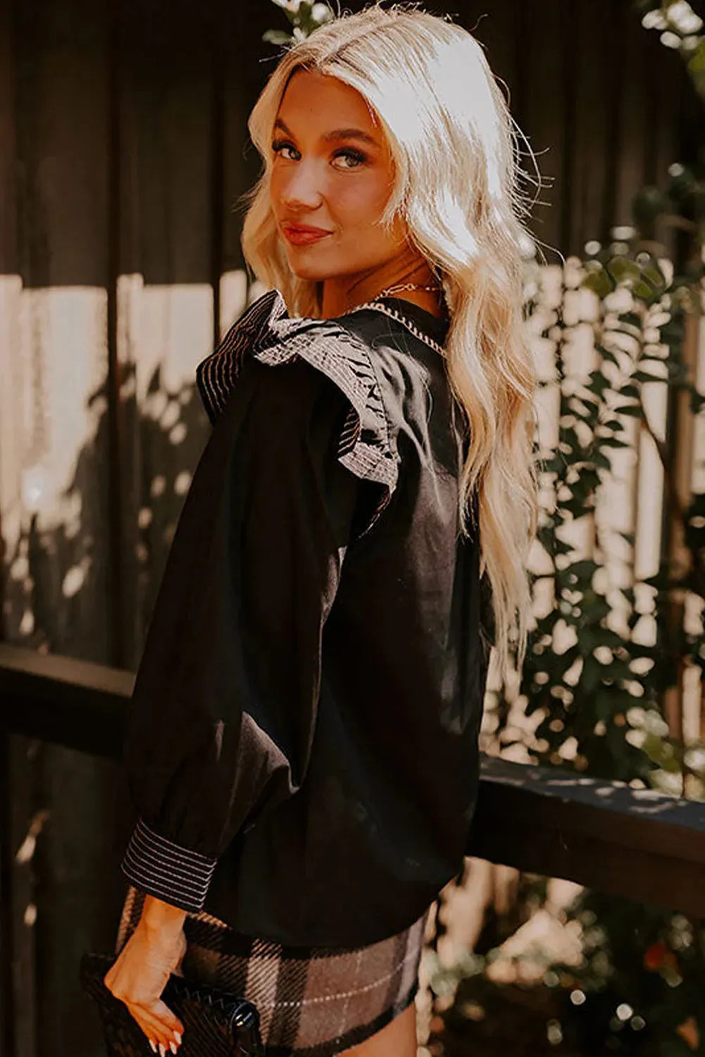 Black women's V-neck blouse with ruffle detailing on the long sleeves and contrast colour stitching.