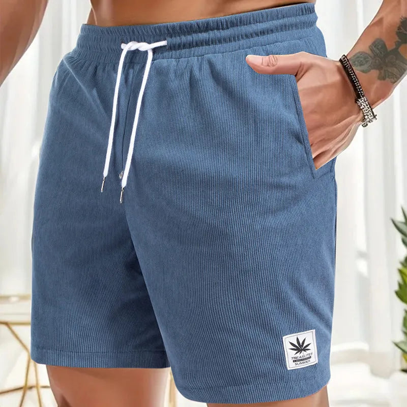 Man wearing grey straight-cut elastic drawstring summer shorts on a beach.