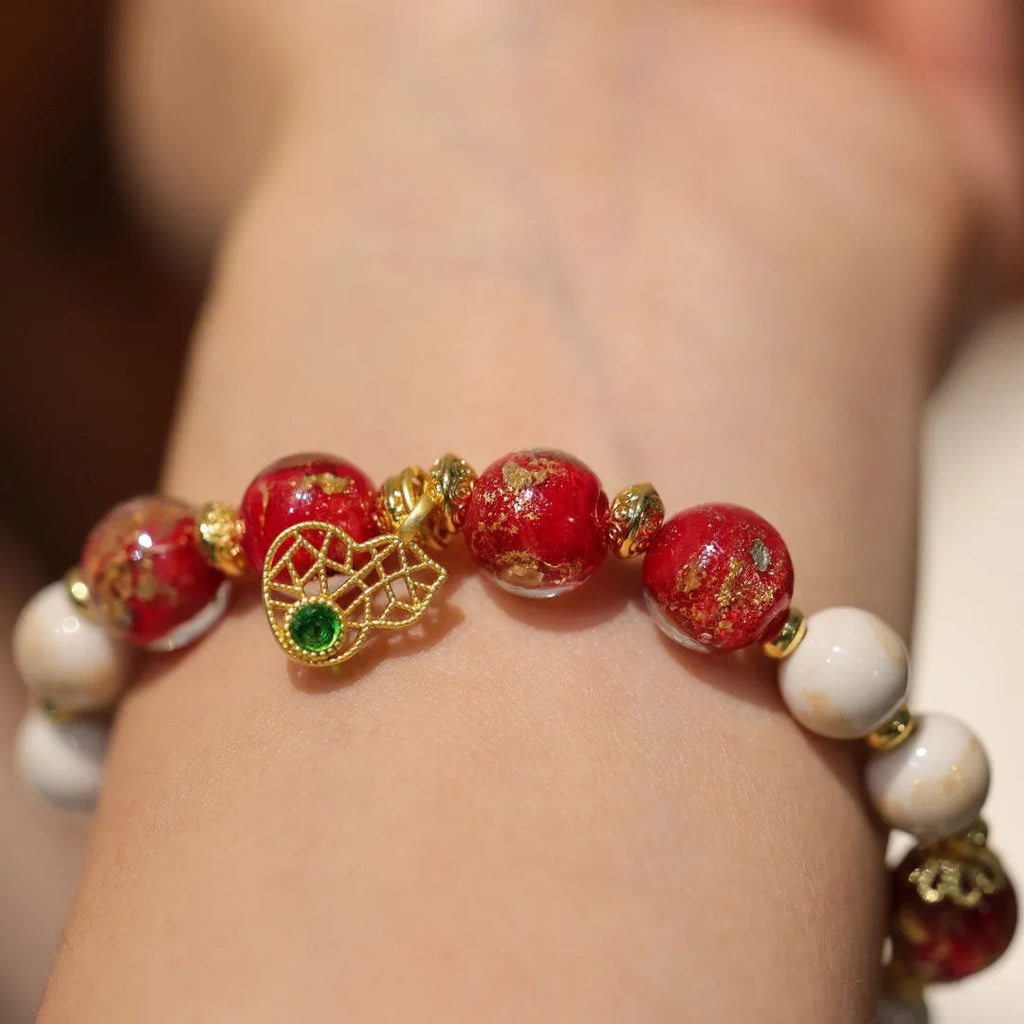 Women's ethnic style bracelet with gold foil designs on red and pink coloured glass glaze, featuring geometric shapes and charms.