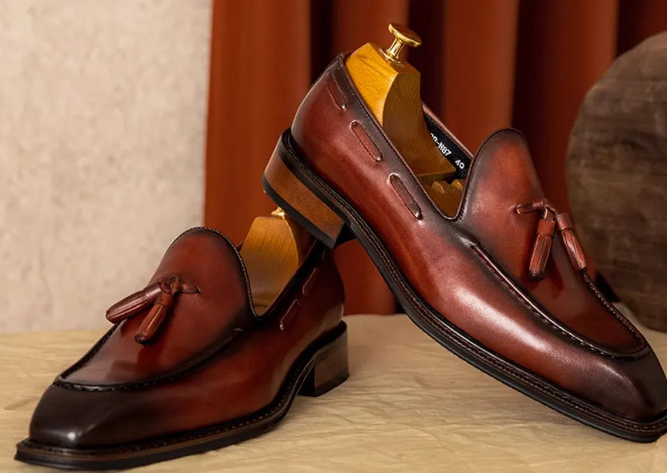 Men's black genuine leather loafers with fringe detail and a rubber sole, shown from a side angle.