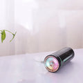 Black and white portable USB rechargeable car humidifier with colourful LED lights on a desk.