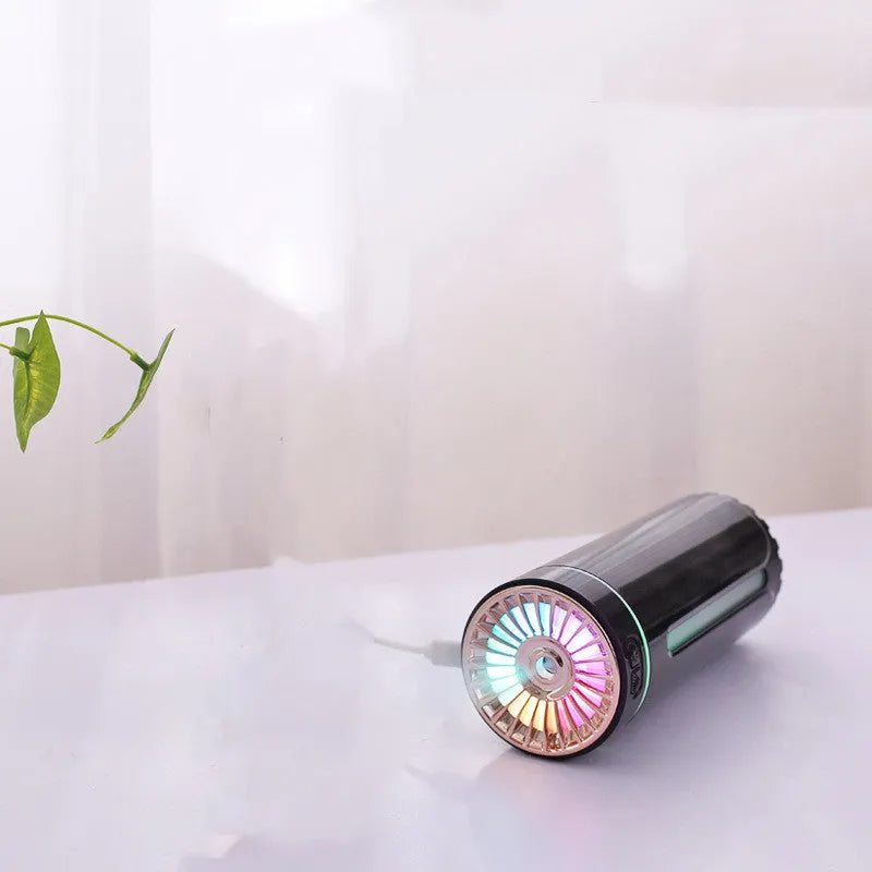 Black and white portable USB rechargeable car humidifier with colourful LED lights on a desk.