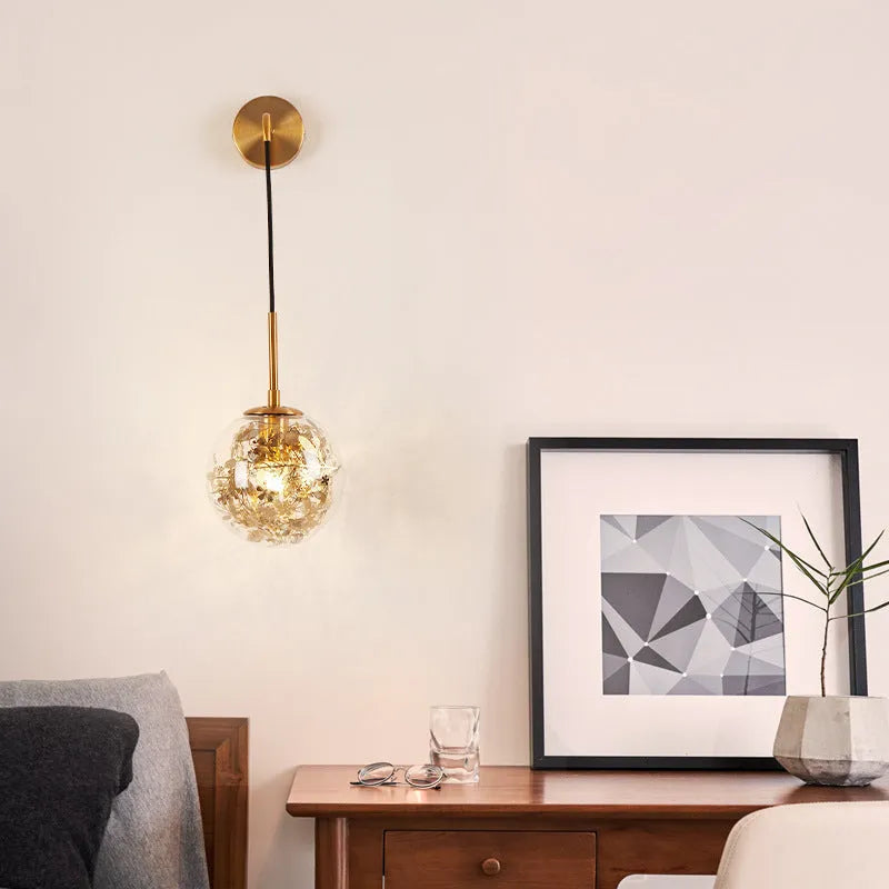 Modern round glass wall lamp in golden flower finish mounted beside a bed.