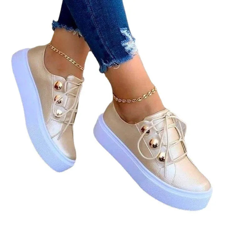 Women's white lace-up flat sneakers with silver rivet detail on the low upper and round toe.