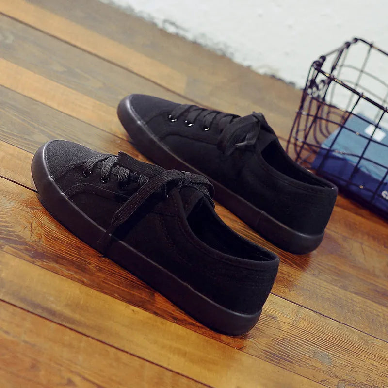 All-black women's low-top canvas shoes with lace-up front and flat rubber sole.