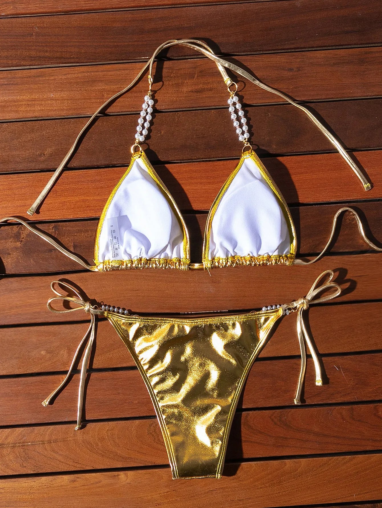 Gold bronzing effect women's halter neck bikini with lace-up back and pearl chain detail on mannequin