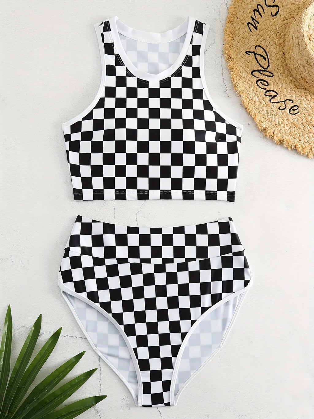 Adult woman wearing a black and white checkerboard print one-piece swimsuit with suspender straps and a backless sporty design.
