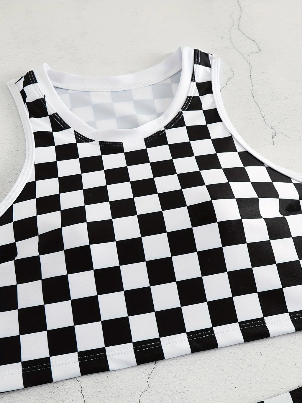 Adult woman wearing a black and white checkerboard print one-piece swimsuit with suspender straps and a backless sporty design.