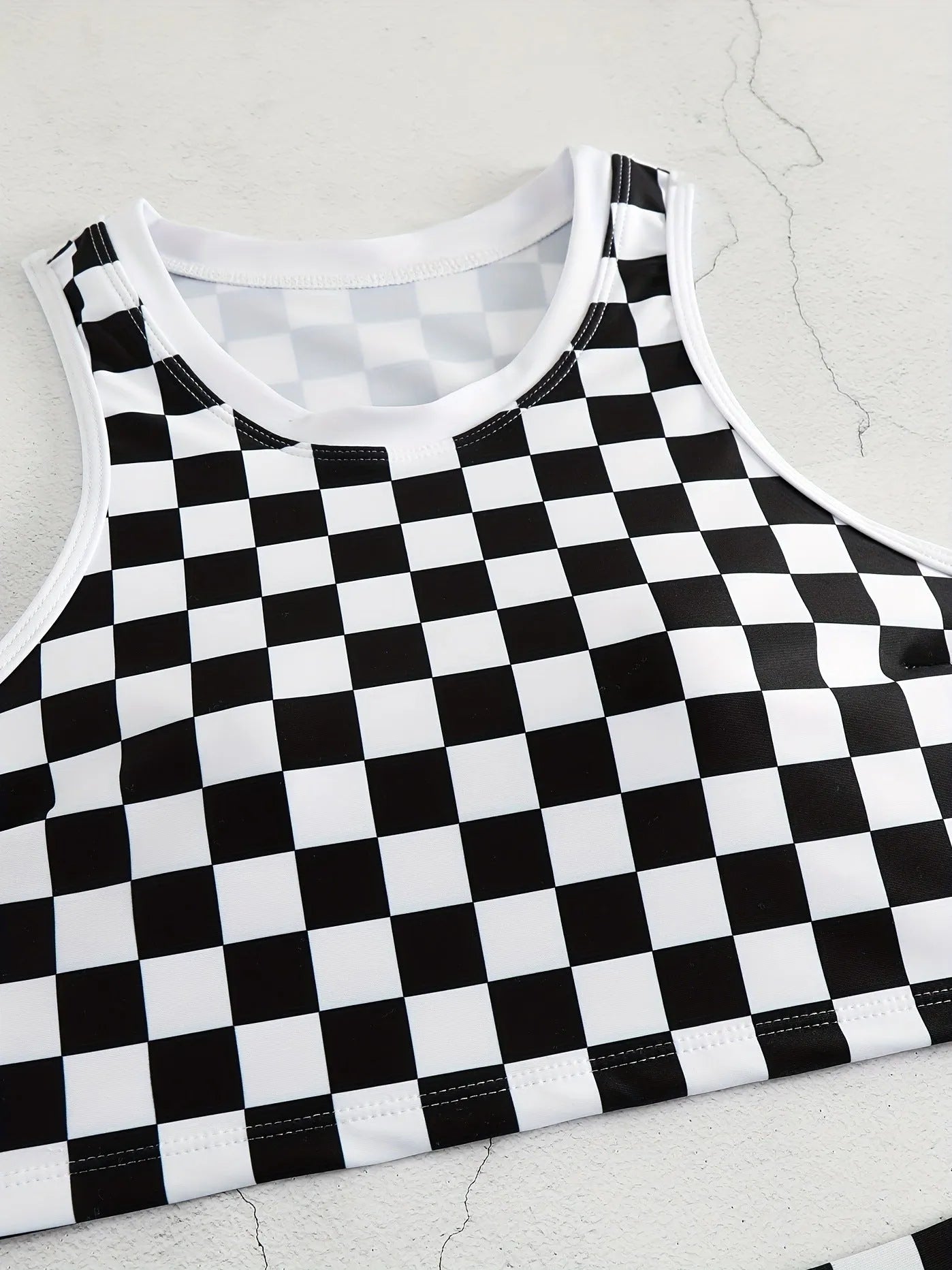 Adult woman wearing a black and white checkerboard print one-piece swimsuit with suspender straps and a backless sporty design.