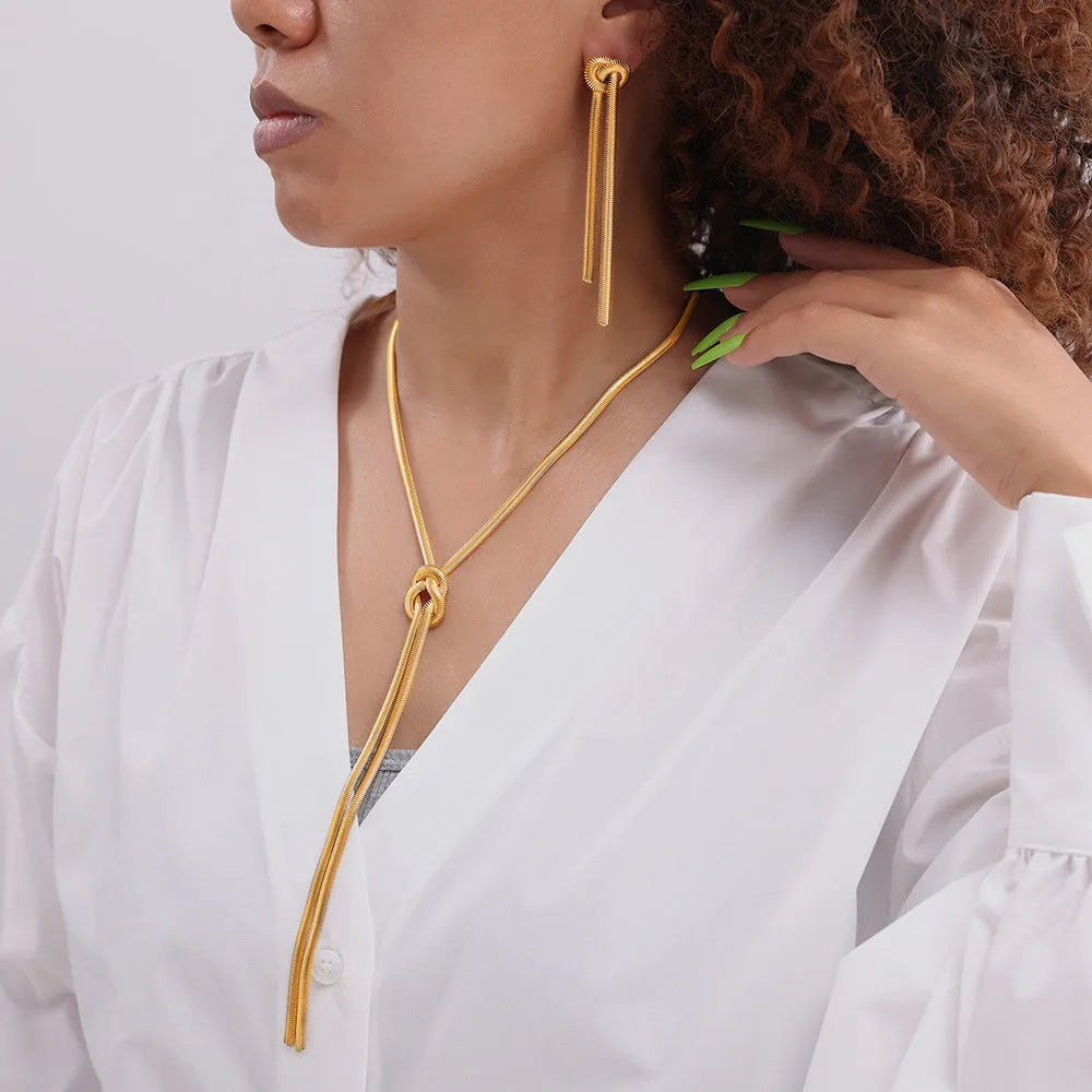 Gold plated titanium steel necklace with snake chain and knotted tassel pendant, shown with matching earrings.