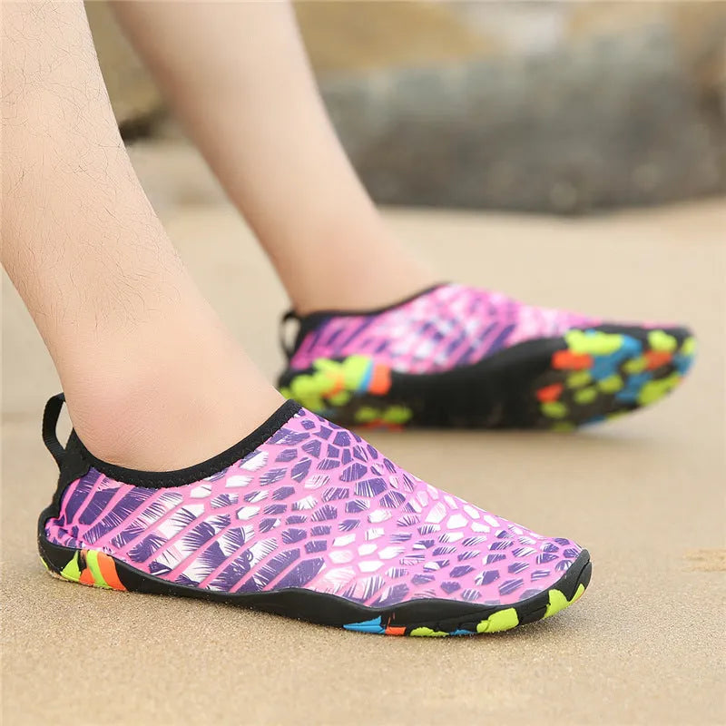 Blue Lycra beach wading shoes with decorative printing, shown on a sandy background