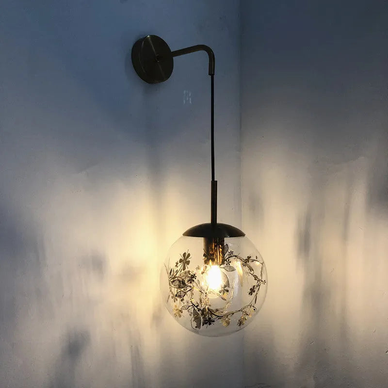Modern round glass wall lamp in golden flower finish mounted beside a bed.