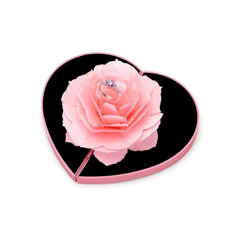 Red 3D heart-shaped plastic ring box with a rotating white rose decoration on top.
