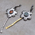 A pair of long, geometric flower-shaped retro earrings in two contrasting metallic colours with an asymmetrical design.
