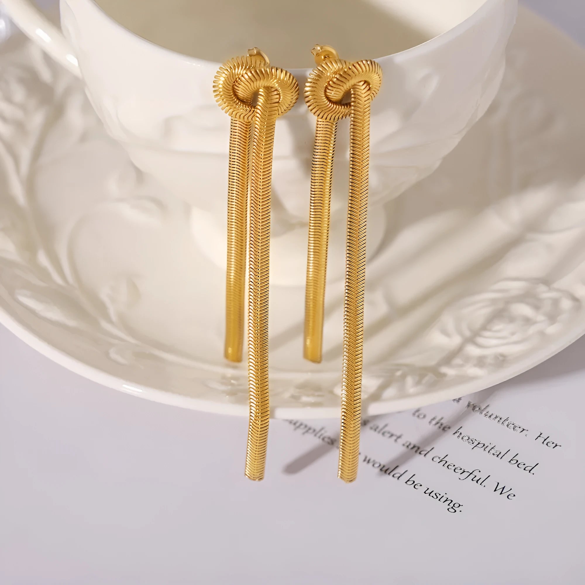 Gold plated titanium steel necklace with snake chain and knotted tassel pendant, shown with matching earrings.