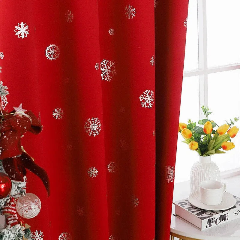 Red snowflake pattern shade cloth curtain with iron hoops hanging on a rod against a window.