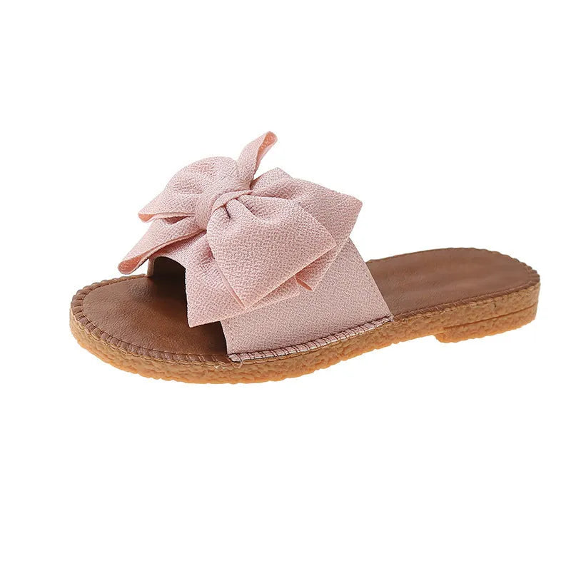 Women's beige suede slip-on sandals with a bow and flat soft rubber sole.