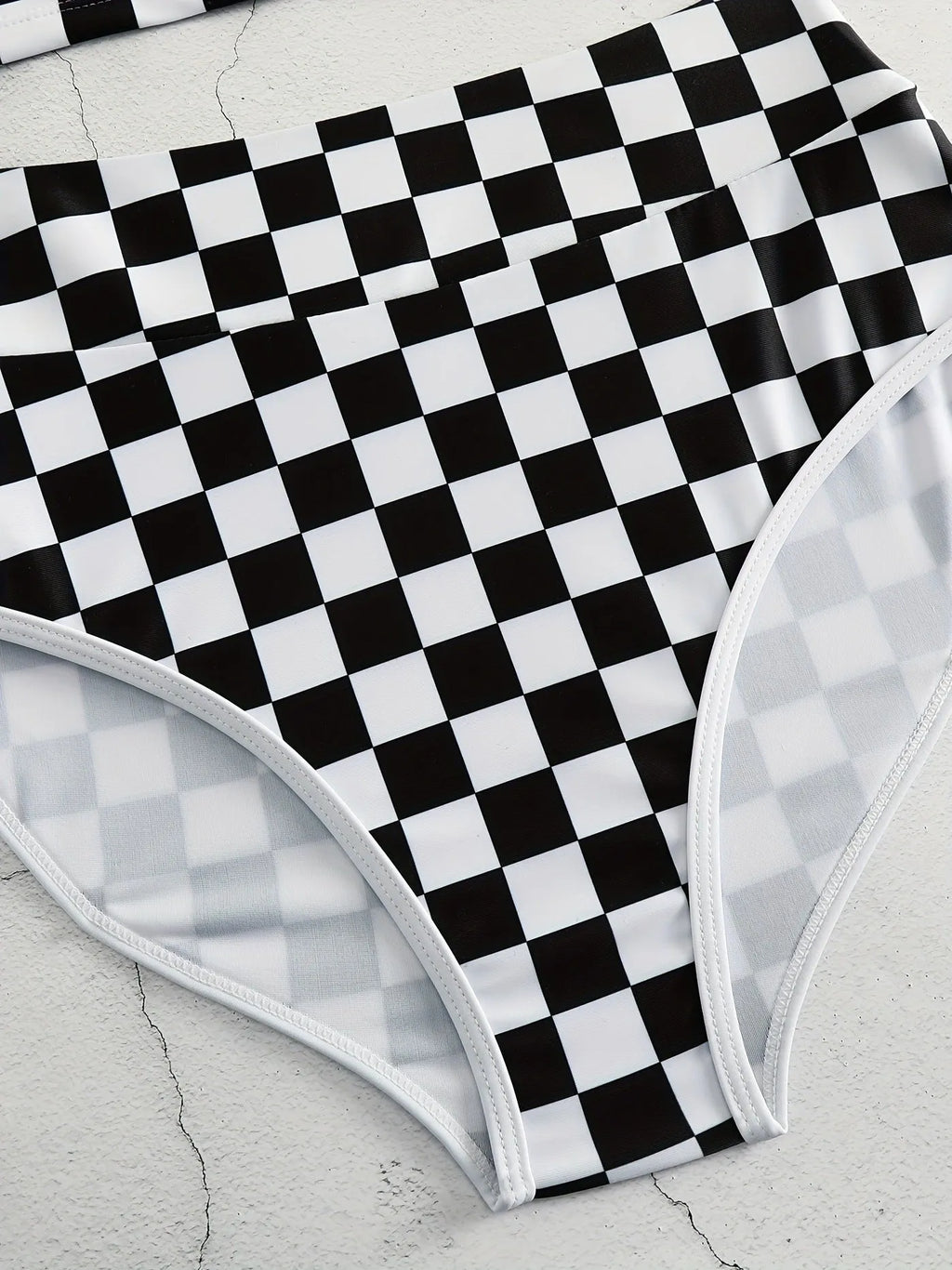 Adult woman wearing a black and white checkerboard print one-piece swimsuit with suspender straps and a backless sporty design.