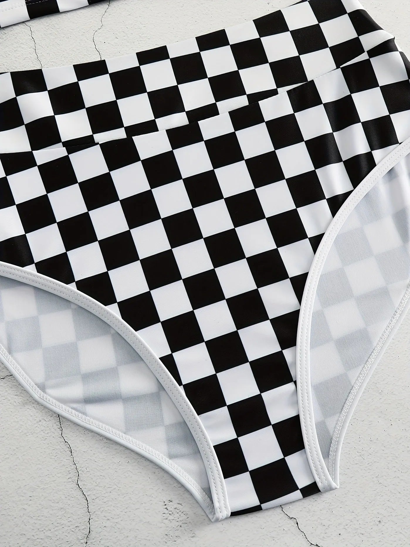 Adult woman wearing a black and white checkerboard print one-piece swimsuit with suspender straps and a backless sporty design.