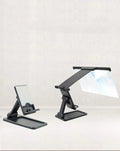 Black detachable mobile phone screen amplifier and folding holder shown on a desk next to a phone.