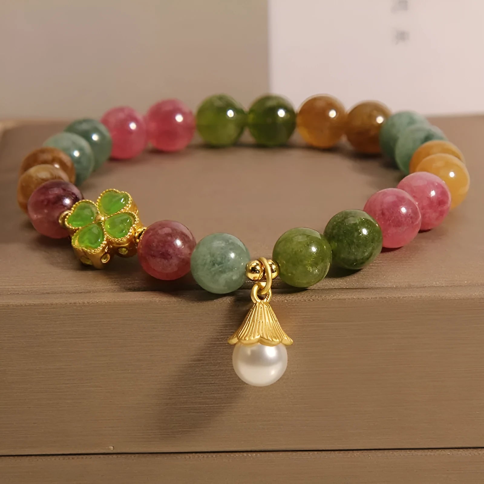 Natural colour tourmaline bracelet with four-leaf clover pearl pendant on wrist.