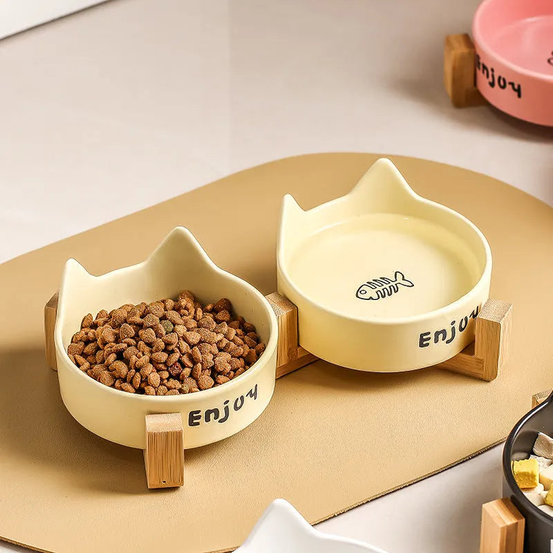 Porcelain cat bowl with cat ear handles in a wooden anti-tumble frame, showing paw print design.