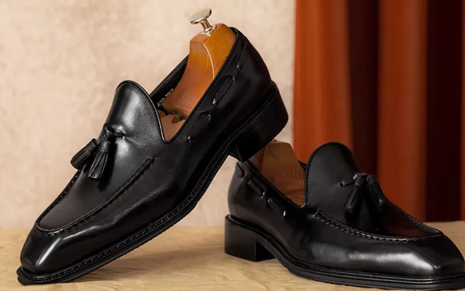 Men's black genuine leather loafers with fringe detail and a rubber sole, shown from a side angle.