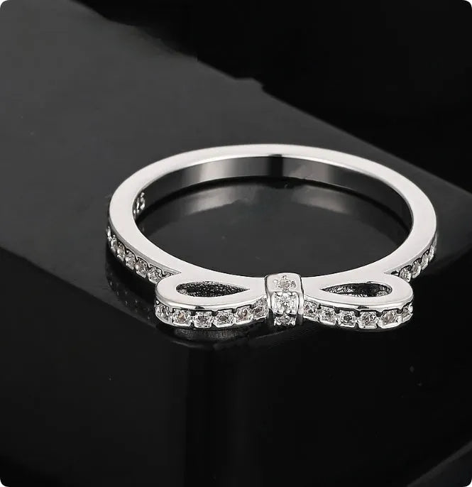A silver couple-style ring with a bow shape decorated with rhinestones and zircon crystals.