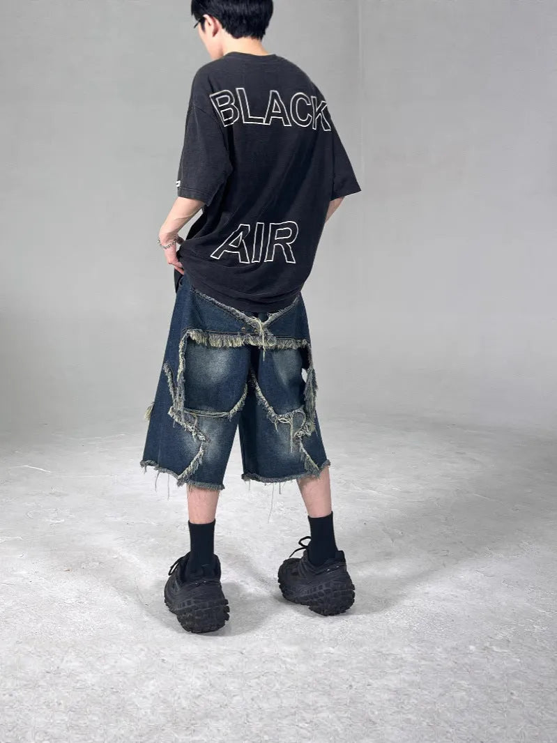 Blue denim shorts with a frayed hem and a large five-pointed star design on the leg, shown on a model.
