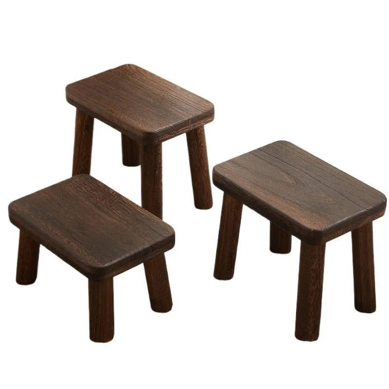 A rustic distressed wooden stool with bracket legs, used as a shoe changing bench in a hallway.
