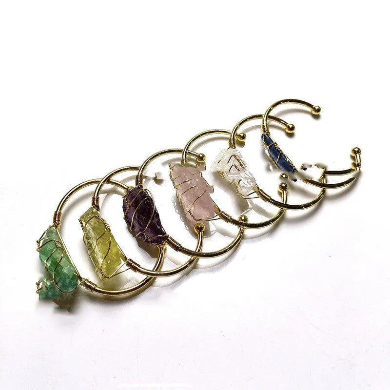 Natural rough stone crystal bracelet with gold geometric winding on a wrist.