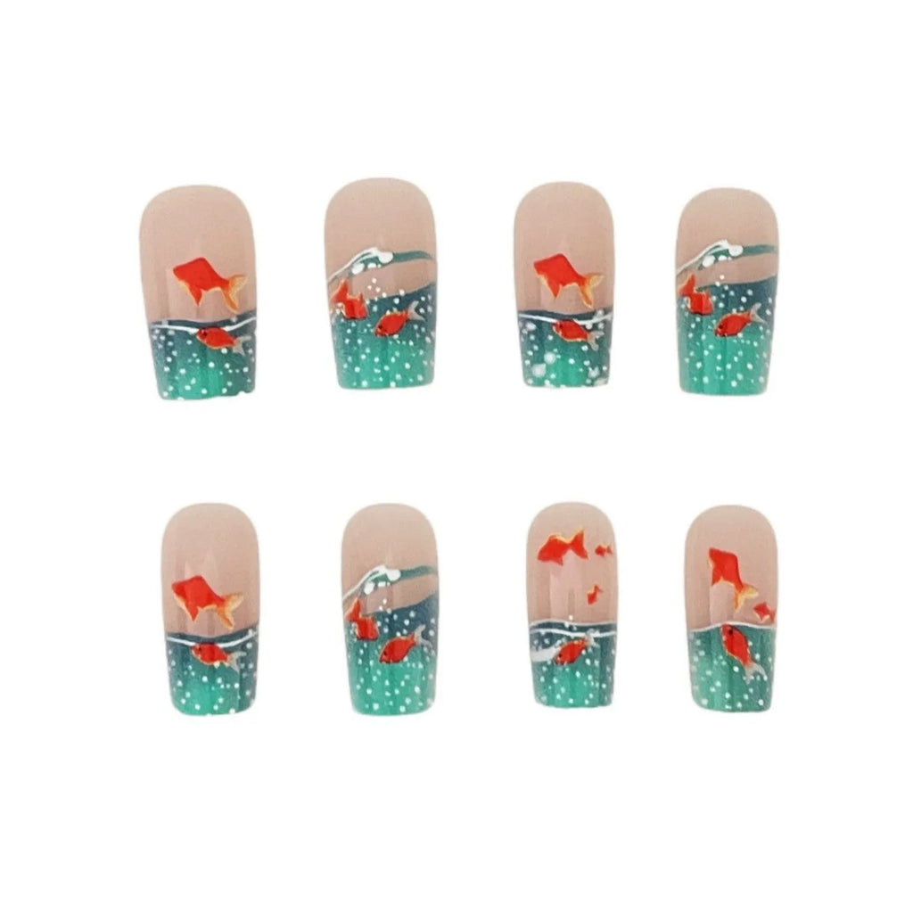 Mid-square blue glaze goldfish nail art pieces with armour design and jelly glue finish on a table