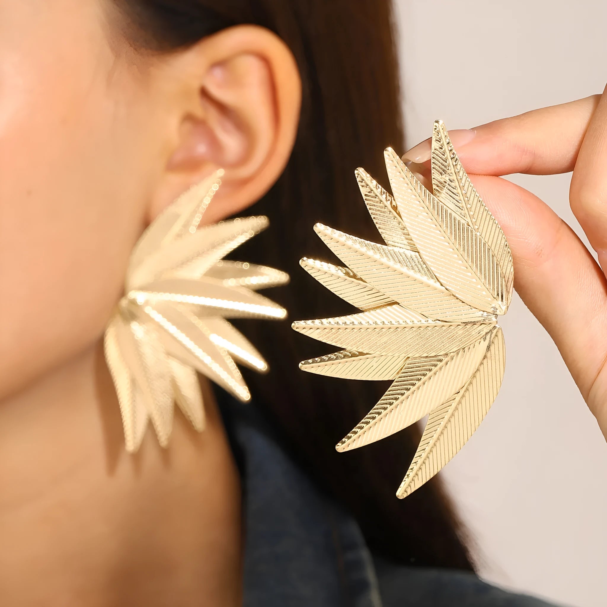A pair of gold alloy drop earrings shaped like leaves, lying on a surface.