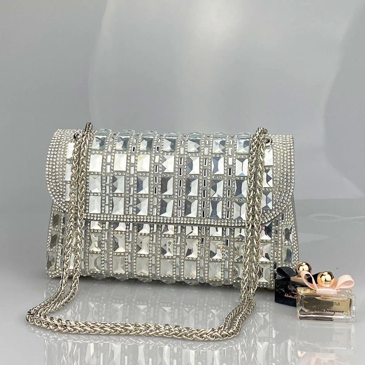 Silver rhinestone chain clutch bag with square shape and internal phone pocket on a table.