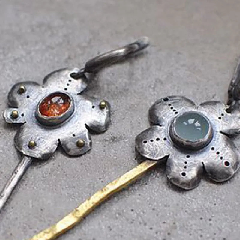 A pair of long, geometric flower-shaped retro earrings in two contrasting metallic colours with an asymmetrical design.