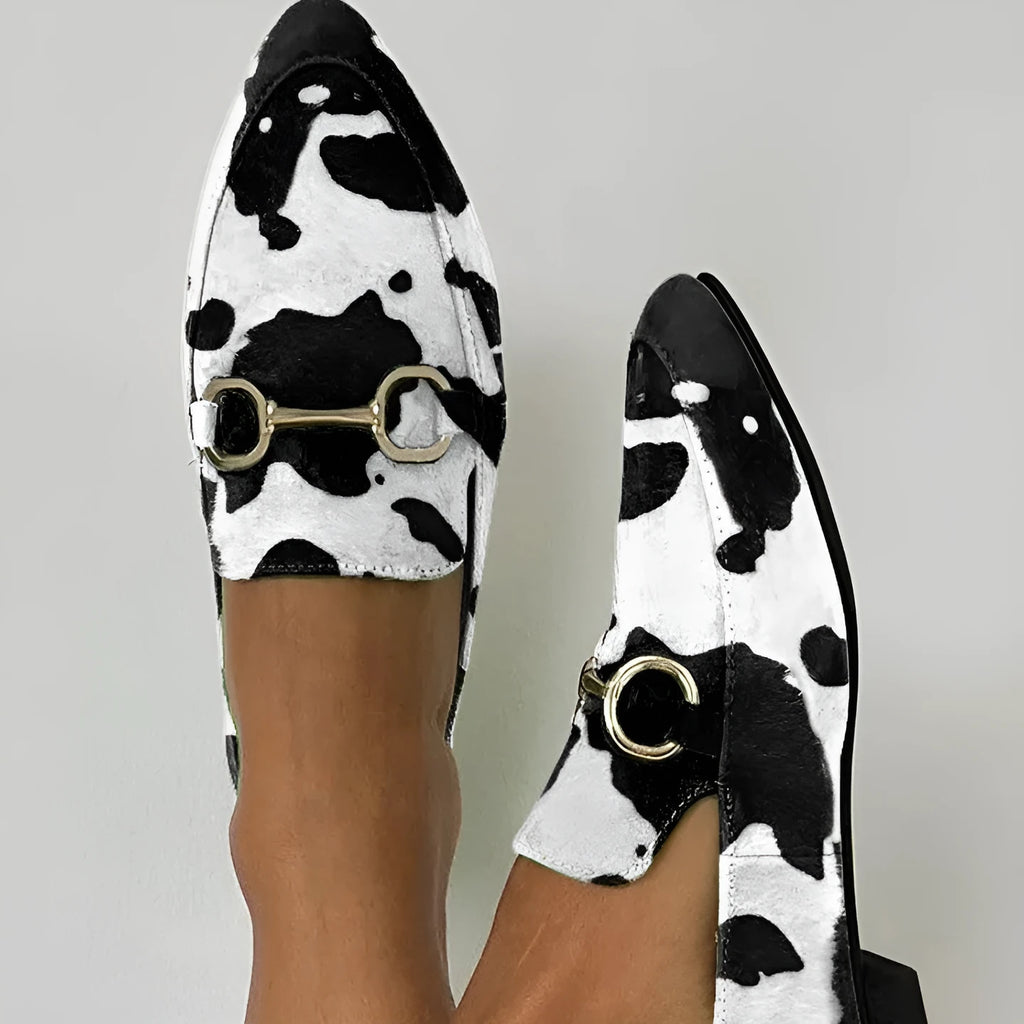 Women's black and white cow pattern pointed-toe mules with flat square heel on a neutral background