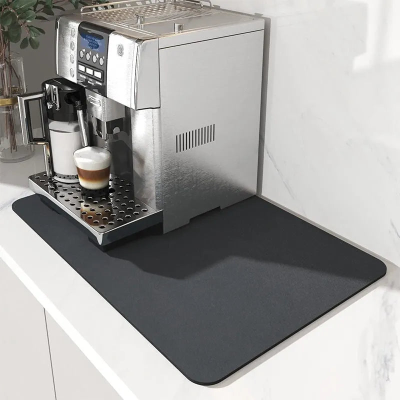 Square black kitchen drain mat with rubber backing placed under coffee machine on countertop