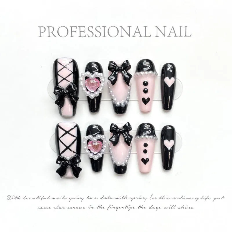 Hand-painted black artificial nails with pink hearts and a bow design, showing mid-length cat's eye style.