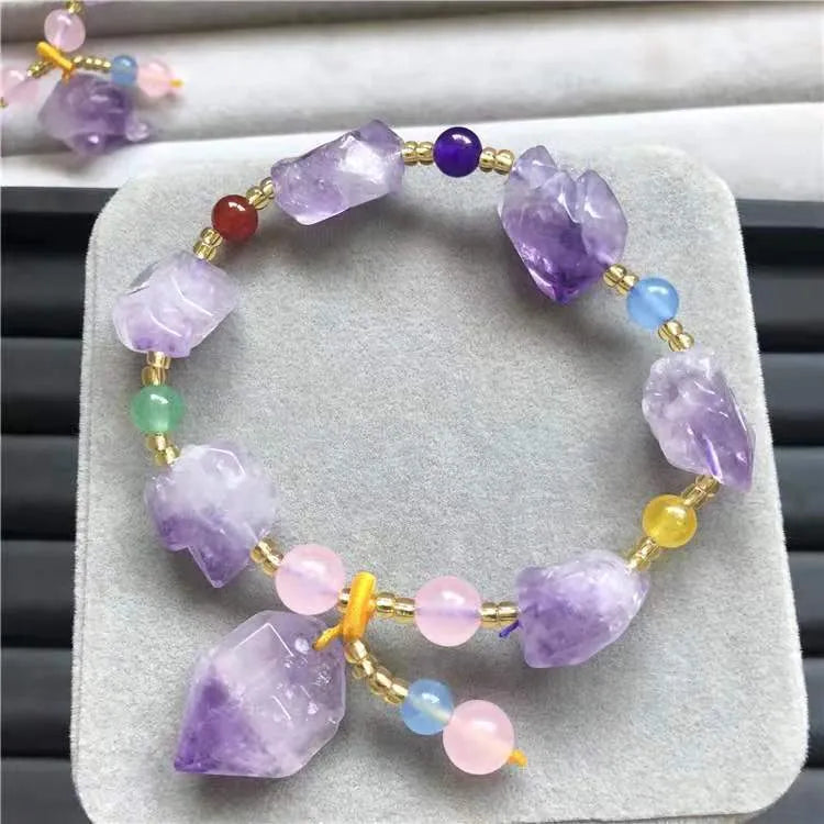Close-up of a women's bracelet with natural shaped amethyst beads and a silver fu charm on a white background.