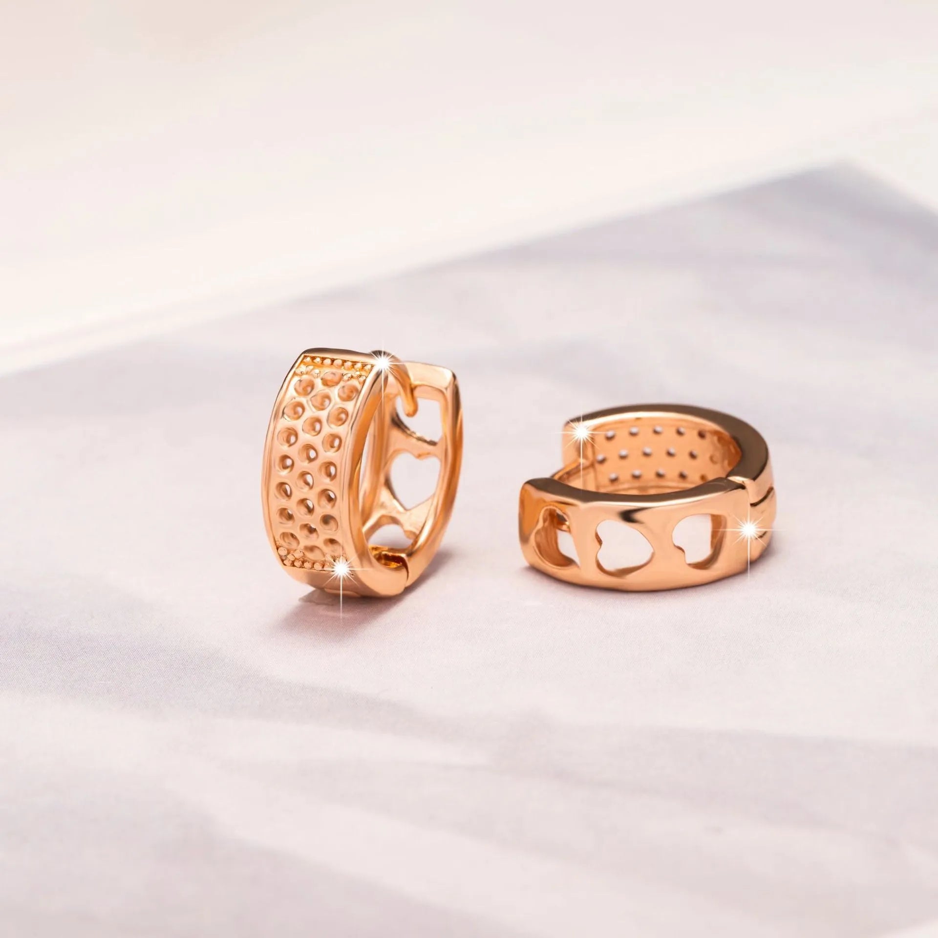 Rose gold women's earrings with three hollowed heart charms on a circular setting.